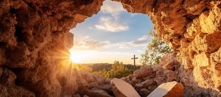 A serene view from a cave with a cross and sunset in the background. photo