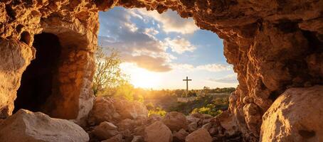 View from a cave opening towards a cross at sunset. photo