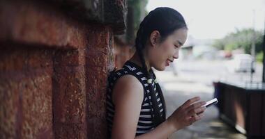Handheld side view shot, Attractive woman leaning against a wall on a sidewalk enjoying the city view while using a map app to find directions on mobile phone. video