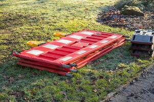 Red and white crowd control barriers laying on grass next to sidewalk photo