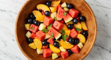 An overhead view of a colorful fruit salad served in a wooden bowl, featuring a mix of watermelon, grapes, peaches, and oranges, garnished with fresh mint leaves. photo
