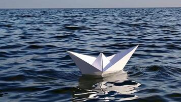 Origami paper boat floating on calm blue water surface, creating gentle ripples and reflections, evoking feelings of tranquility and adventure video