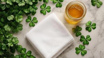 A blank white towel laying with a golden honey jar and clovers lying around it. 6 photo