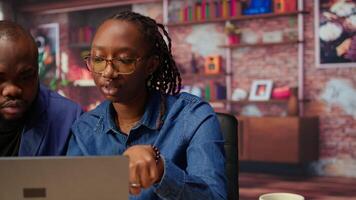 Freelancers filling in spreadsheets on laptop by entering data from report papers, analyzing figures at the end of the month. African american man and woman working from home. Camera A. video