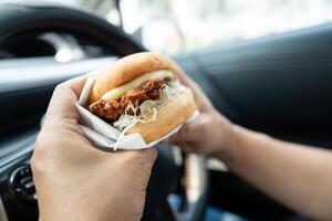 Asian lady holding hamburger to eat in car, dangerous photo