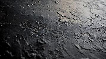 Textured dark surface featuring an uneven and rough appearance, creating a pattern of depth with varying degrees of light reflection. photo