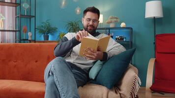 Young man relaxing interesting book turning pages smiling enjoying literature taking a rest on sofa video
