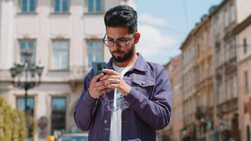 Indian man use smartphone typing text messages browsing internet finishing work looking at camera video