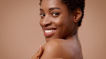 A young African American woman with short hair shows her playful side while smiling. She appears relaxed and confident, highlighting her natural beauty in a minimalistic setting. video