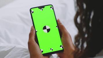 Cozy bedroom features a millennial woman in a bathrobe, focused on her smartphone with blank screen. Soft bedding creates a relaxing atmosphere while she enjoys her leisure time at home. video