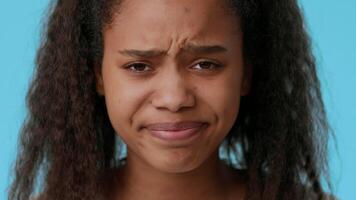 A teenage girl with beautiful features displays a range of emotions, her brows furrowed and mouth slightly open, isolated against a bright blue backdrop that enhances her expression. video