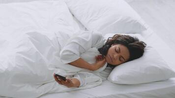 A millennial woman of African descent peacefully sleeps in a bright white bedroom. Her warm bathrobe adds comfort as she lays on soft pillows, embracing a serene moment of relaxation. video