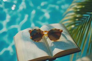 Sunglasses resting on open book by sparkling blue pool photo