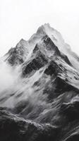 Snowy mountain peak emerging from misty clouds in black and white photo