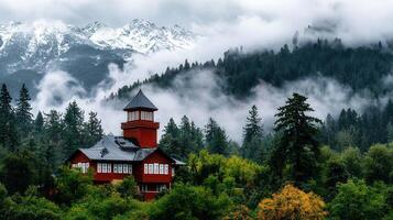 Majestic Red House nestled in lush green forest with snow capped mountains and misty clouds creating a serene atmosphere photo