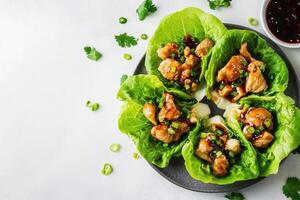 A plate of lettuce wraps filled with chicken and sauce, garnished with green onions. photo