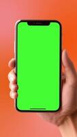 Animated of a person's hand holding a smartphone with a green screen, ideal for editing or using chroma key in videos on a orange vertical background