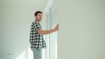 Man in checkered shirt leans checking wall alignment in new built apartment. Homeowner inspecting construction quality of new home. Concept of renovation quality control and home evaluation video