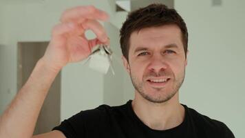 Happy man holding keys to his new apartment. Cheerful male home owner smiling while holding keys in bright, modern interior. Concept of purchase new home and real estate video