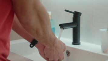 Close-up of man washing hands under running water in bathroom sink with black faucet. Hygiene, cleanliness and self-care morning routine concept video