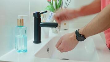 Close-up of man washing hands under running water in bathroom sink with black faucet. Hygiene, cleanliness and self-care morning routine concept video