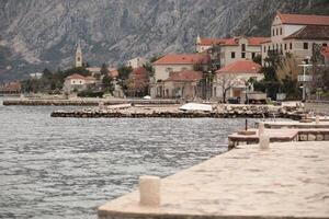 Coastal view of serene waterfront with stone pier and charming buildings in the background of Montenegro mountains photo