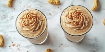 Creamy peanut butter smoothies topped with whipped cream and sprinkled with cinnamon on a marble countertop photo