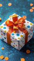 Colorful gift box with polka dots and ribbon on blue background surrounded by confetti photo