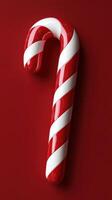 Red and white striped candy cane with glossy finish resting on a red background photo