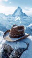 Snowy mountain peak with a weathered cowboy hat resting on a rock under a clear blue sky photo