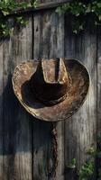 Old cowboy hat displayed on wooden wall adorned with greenery, showcasing rustic charm and western heritage photo
