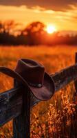 Sunset casts warm glow on cowboy hat resting on rustic fence in golden field photo