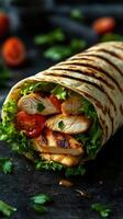 Freshly made grilled chicken wrap with vegetables and herbs on a rustic black surface photo