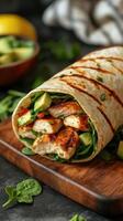 Delicious grilled chicken wrap with fresh avocado and spinach on a wooden board photo