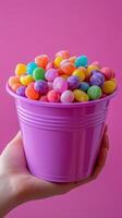 Colorful candy-filled bucket held in hand against a vibrant pink background captures the joy of sweets photo