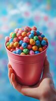 Brightly colored candy in a pink bucket held by a hand against a soft blurred background photo