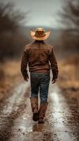 Cowboy walks down muddy rural path surrounded by muted landscape during overcast afternoon photo