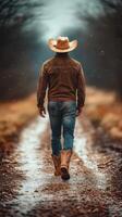 Cowboy walking along a winding dirt path in a rural setting during a chilly autumn day with light snowfall photo