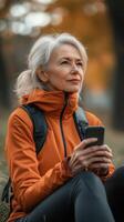 Older woman in an orange jacket enjoys nature while checking her mobile phone during a peaceful autumn day photo