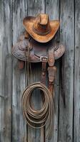 Rustic saddle and cowboy hat hanging on weathered wooden wall in a barn setting at dusk photo