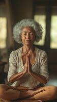 Older woman practicing meditation indoors with hands in prayer position and calm expression photo