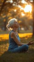 Senior woman practicing yoga and meditating at sunset in a serene park setting photo