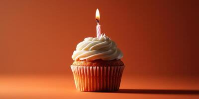 Cupcake with cream frosting and lit candle on an orange background for birthday celebration photo