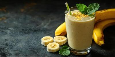 Creamy banana smoothie served in a glass with fresh mint and sliced bananas on a dark textured background photo