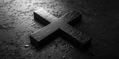 Black wooden cross lies on a textured surface with water droplets reflecting light in a dimly lit setting photo