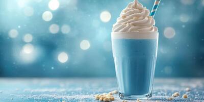 Refreshing blue milkshake topped with creamy whipped cream and a striped straw served in a glass on a sparkling blue background photo