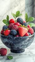 Freshly picked berries in a decorative bowl on a marble surface with leafy accents photo