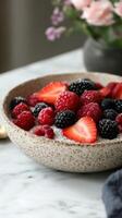 Delicious bowl of fresh berries with texture on marble table with flowers in background photo