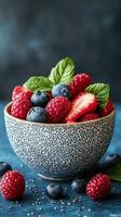 Fresh berries in a textured bowl with mint leaves arranged on a blue surface with chia seeds scattered around photo
