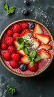 Colorful berry smoothie bowl served in a rustic bowl garnished with fresh fruits and mint leaves on dark background photo